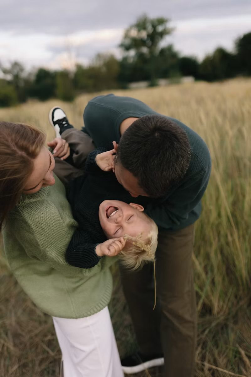 Parents laughing with their young son in a golden field