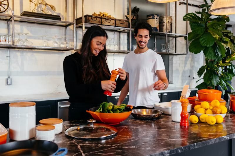 Two people laughing while cooking together in a bright kitchen